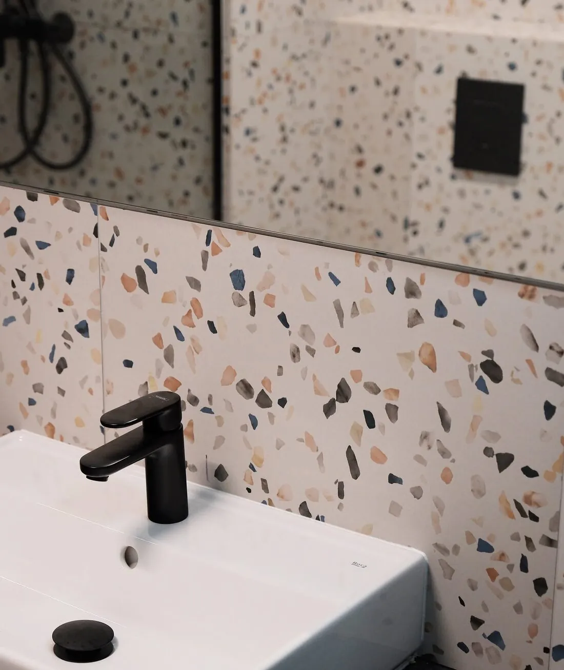 Umywalka z czarną baterią na tle terrazzo